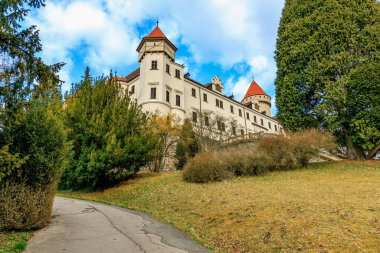 Yeşilliklerle çevrili kırmızı taretleri olan görkemli bir kale. 17 Mart 2025, Konopiste Şatosu, Çek Cumhuriyeti.