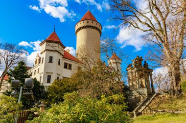 Kırmızı kuleleri ve gür ormanlık alanda taş duvarları olan görkemli ortaçağ kalesi. 17 Mart 2025, Konopiste Şatosu, Çek Cumhuriyeti.