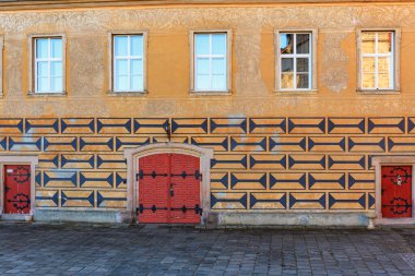 Geometrik desenli ve kırmızı kapılı tarihi mimari cephe. 16 Mart 2025, Hruba Skala Şatosu, Çek Cumhuriyeti.