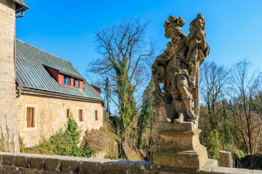 Güneşli bahçe ortamında, kır evinin yanındaki tarihi taş heykel. 16 Mart 2025, Hruba Skala Şatosu, Çek Cumhuriyeti.
