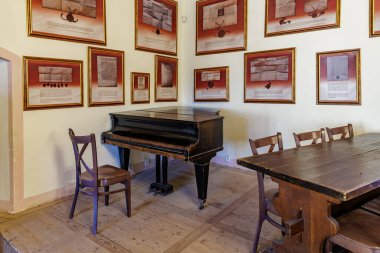 Tarihi odada çerçeveli sanat eserleri olan klasik piyano ve ahşap sandalyeler. 18 Mart 2025, Madalyon, Çek Cumhuriyeti.