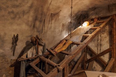 Ortaçağ işkence sahnesinde loş aydınlatılmış zindan sergisinde bir adam vardı. 18 Mart 2025, Madalyon, Çek Cumhuriyeti.