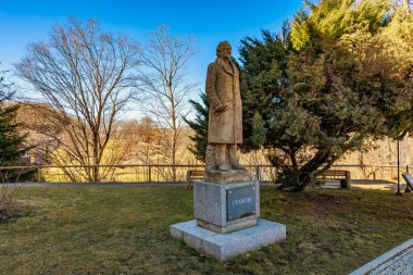 Goethe 'nin parktaki taş heykeli ağaçlar ve açık mavi gökyüzü ile birlikte. 18 Mart 2025, Madalyon, Çek Cumhuriyeti.