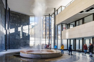 Modern bir bina lobisinde ziyaretçileri olan kapalı bir jeotermal çeşme. 18 Mart 2025, Karlovy Vary, Çek Cumhuriyeti.