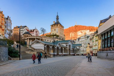 İnsanlarla dolu tarihi kasaba meydanı ve gün batımında manzaralı mimari. 18 Mart 2025, Karlovy Vary, Çek Cumhuriyeti.