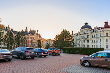 Gün batımında otoparkta arabalarla tarihi Avrupa mimarisinin manzarası. 18 Mart 2025, Karlovy Vary, Çek Cumhuriyeti.