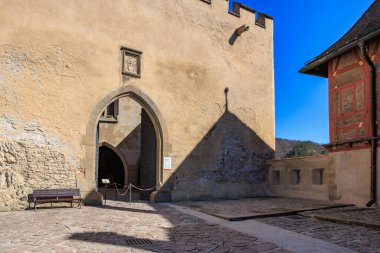 Mavi gökyüzünün altında gölgeli ortaçağ taş kale girişi. 19 Mart 2025, Karlstejn, Çek Cumhuriyeti.