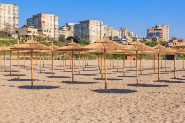 Saman şemsiyeli kumsal ve parlak güneş ışığında şehir silueti. 4 Mayıs 2025 Romanya.