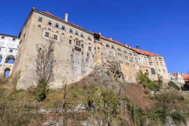Mavi gökyüzünün altındaki kayalık kayalıklarda ortaçağ Avrupa şatosu. 20 Mart 2025, Cesky Krumlov, Çek.