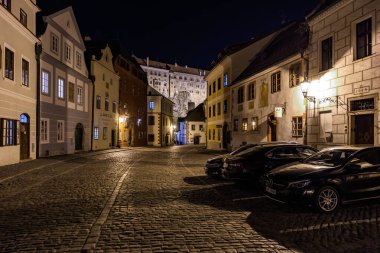 Gece vakti tarihi şehir caddesinin kaldırım taşları ve arabalarla manzarası. 20 Mart 2025, Cesky Krumlov, Çek.