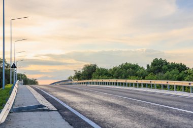 Boş karayolu köprüsü üzerinde gün batımı yemyeşil ağaçlar ve açık gökyüzü.