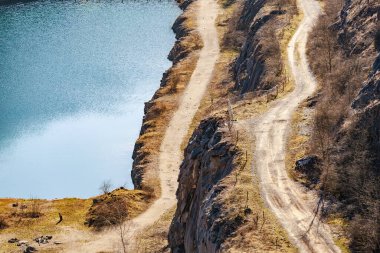 Uçurumun kenarındaki toprak yolun ve mavi gölün hava manzarası.