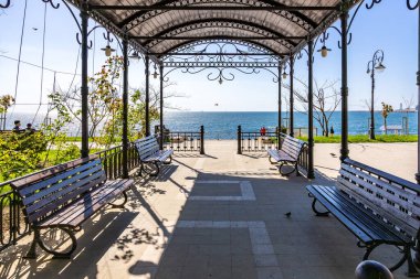 Deniz kenarında güneşli gökyüzünün altında bankları olan okyanus manzaralı bir çardak. 3 Mayıs 2025 Romanya.