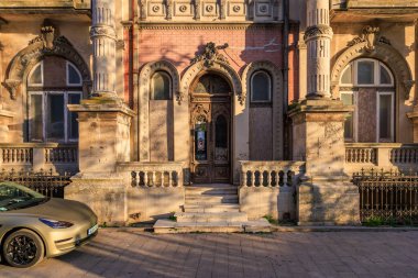Süslü detaylarla dolu tarihi Avrupa malikanesi cephesi ve gün batımında park edilmiş bir araba. 3 Mayıs 2025 Romanya.