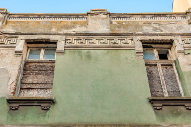 Tahta pencereli terk edilmiş binanın harap olmuş yeşil cephesi. 3 Mayıs 2025 Romanya.