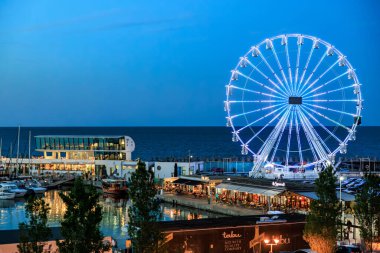 Alacakaranlıkta deniz kenarında liman manzaralı bir dönme dolap. 3 Mayıs 2025 Romanya.