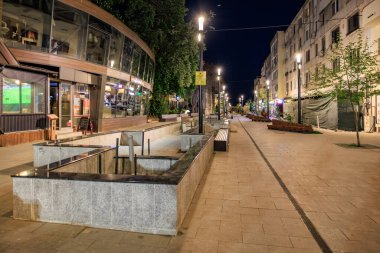 Modern şehir gece manzarası aydınlık dükkanları ve bankları olan boş yaya sokağı. 3 Mayıs 2025 Romanya.