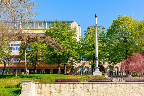 Baharda güneşli şehir parkı, banklar ve lamba direği. 3 Mayıs 2025 Romanya.