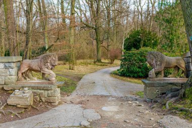 Sakin kış ormanı manzarasında patikayı koruyan taş aslan heykelleri. 17 Mart 2025, Konopiste Şatosu, Çek Cumhuriyeti.