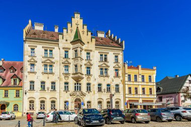 Güneşli bir günde mimari binalar ve park edilmiş arabalarla tarihi kasaba meydanı. 18 Mart 2025, Madalyon, Çek Cumhuriyeti.