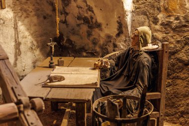 Yaşlı beyaz erkek keşiş tarihi taş odada yazıyor. 18 Mart 2025, Madalyon, Çek Cumhuriyeti.