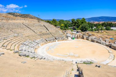 Dairesel bir sahnesi ve etrafını saran taş bir duvarı olan büyük taştan bir amfi tiyatro. Sahne boş ve amfitiyatro kumlu bir alanla çevrili. Yunanistan 'ın antik Filippi kentinin kalıntıları