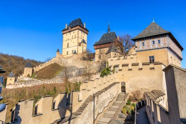 Karlstejn kalesi açık mavi gökyüzü altında tarihi mimarisi ve güçlendirilmiş duvarları ile.