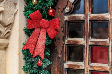 Kırmızı kurdeleli ve kırsal ahşap kapılı Noel çelengi..