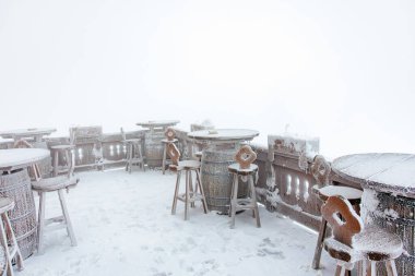 Sisli bir kış gününde karla kaplı kırsal tabloları ve tabureleri olan veranda..