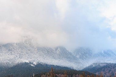 Kış manzarasında bulutlu gökyüzünün altında karla kaplı sıradağlar..