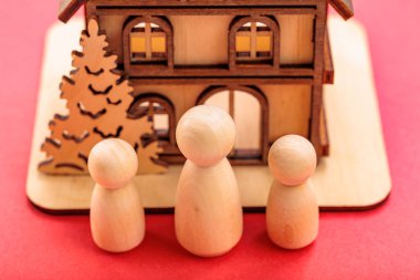 Minyatür ahşap evin önündeki tahta figürler kırmızı arka planda..