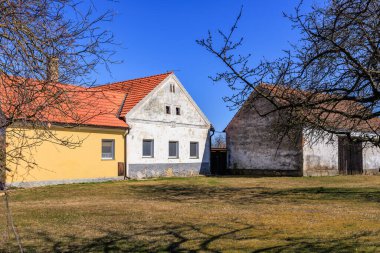 Açık mavi gökyüzü altında iki geleneksel evle taşra manzarası.