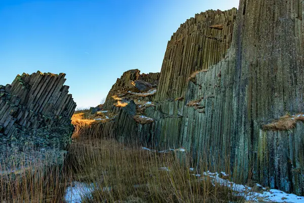 Kayalık arazide mavi gökyüzünün altında görkemli bazalt sütunlar.