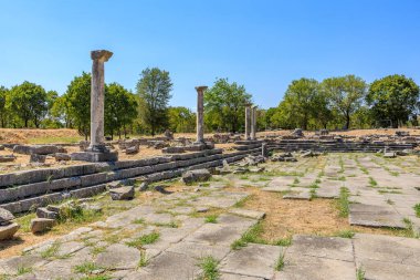 Arka planda birkaç ağaç olan taştan bir geçit. Yürüyüş yolu boş ve gökyüzü temiz. Yunanistan 'ın antik Filippi kentinin kalıntıları