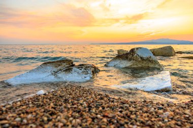 Okyanus sakin ve gökyüzü güzel turuncu bir renktir. Sudaki kayalar beyaz ve su berrak.