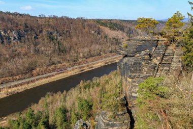 Huzurlu nehre bakan görkemli kumtaşı kayalıkları ve manzaradaki yemyeşil orman.
