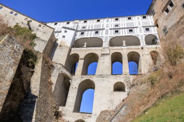 Mavi gökyüzünün altında kemerli destekleri ve kale duvarları olan tarihi taş köprü..