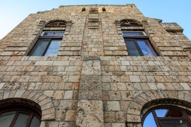 Kemerli pencereleri ve mavi gökyüzü arkaplanı olan tarihi taş bina cephesi.