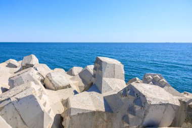 Berrak gökyüzünün altında mavi okyanus kıyı şeridi kenarındaki geometrik beton kırma suyu blokları.