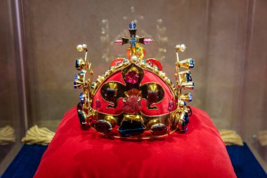 Altın tacı değerli taşlarla süsleyip kırmızı kadife minderde haçla süsleyin..