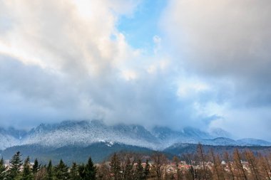 Bulutlu gökyüzünün altında görkemli kar örtülü dağlar.