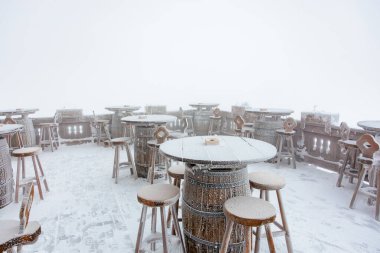 Sisli bir kış gününde varil masalarıyla karla kaplı açık teras..