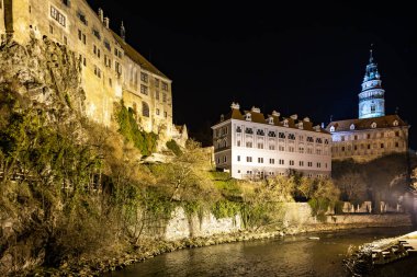 Cesky Krumlov şatosunun yansıtıcı nehirle aydınlatılmış gece görüşü.
