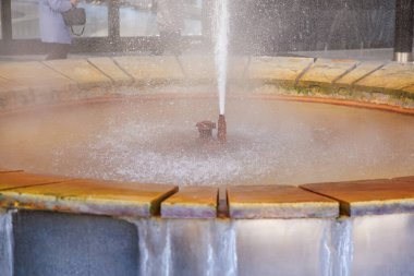 Etrafı taşla çevrili dairesel su çeşmesi ve havaya püsküren merkezi jet, doğal gayzer..