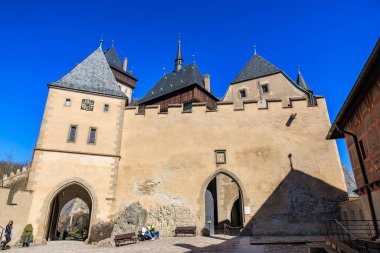Parlak güneş ışığı altındaki görkemli ortaçağ kalesi açık mavi gökyüzüne karşı. 19 Mart 2025, Karlstejn, Çek Cumhuriyeti.