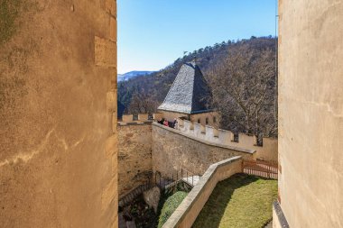 Ortaçağ taş duvarı ve ormanlık tepelere ve mavi gökyüzüne bakan kule. 19 Mart 2025, Karlstejn, Çek Cumhuriyeti.