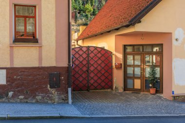 Kırsal binalar ve kırmızı işlemeli demir kapılı Avrupa geçidi. 19 Mart 2025, Karlstejn, Çek Cumhuriyeti.