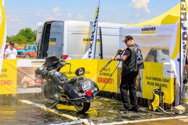 Bir motorcu, motosikletini dışarıdaki temizlik kabininde temizlemek için güçlü bir basınç makinası kullanır. Etkili araç temizleme ürünleri gösteriliyor. 2 Temmuz 2023 Liadoveni Moldova.
