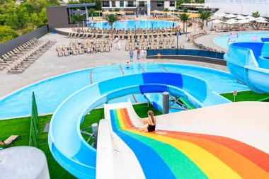 Bir kadın su parkında renkli bir kaydırağın üzerinde kayıyor. Kaydırak bir havuz ve birkaç şezlongla çevrili. 8 Haziran 2024 Balti Moldova