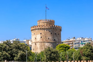 Üzerinde mavi ve beyaz bayrak olan uzun bir kule. Gökyüzü açık ve mavi. Kule ağaçlar ve binalarla çevrilidir. 8 Ağustos 2024 Selanik Yunanistan